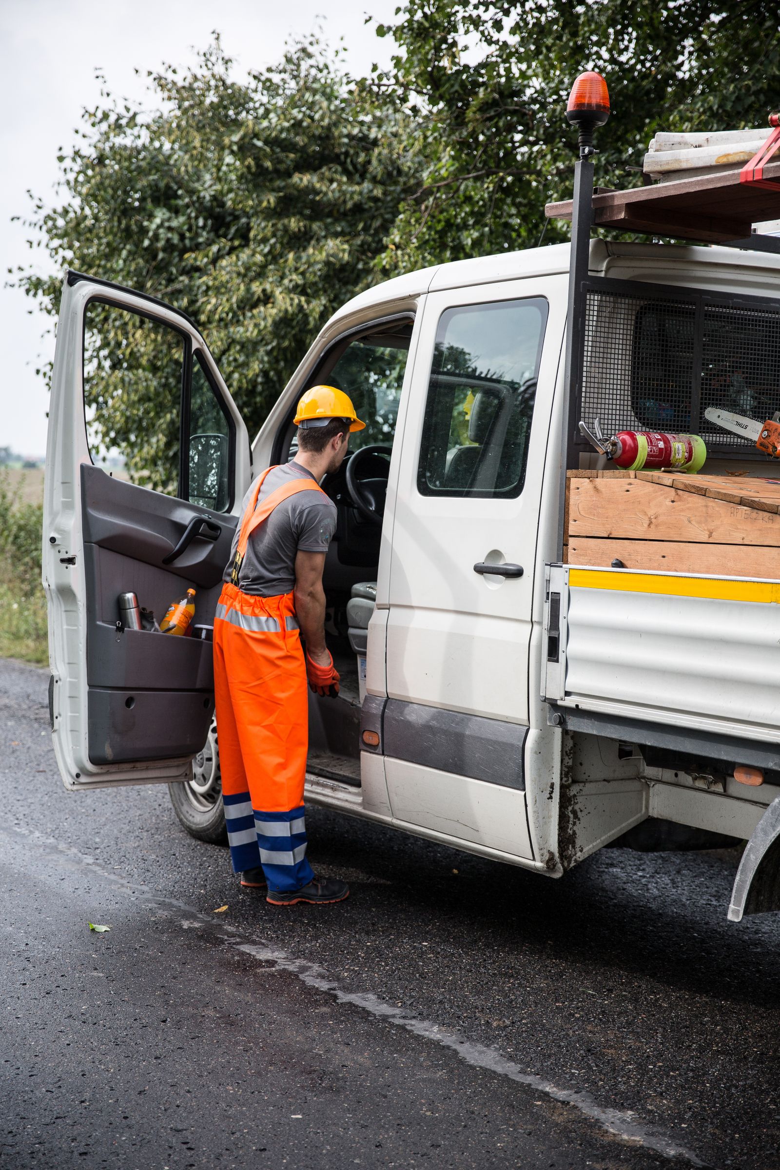Construction worker in hi-vis gear and a hard hat getting into a flatbed work truck loaded with lumber and tools