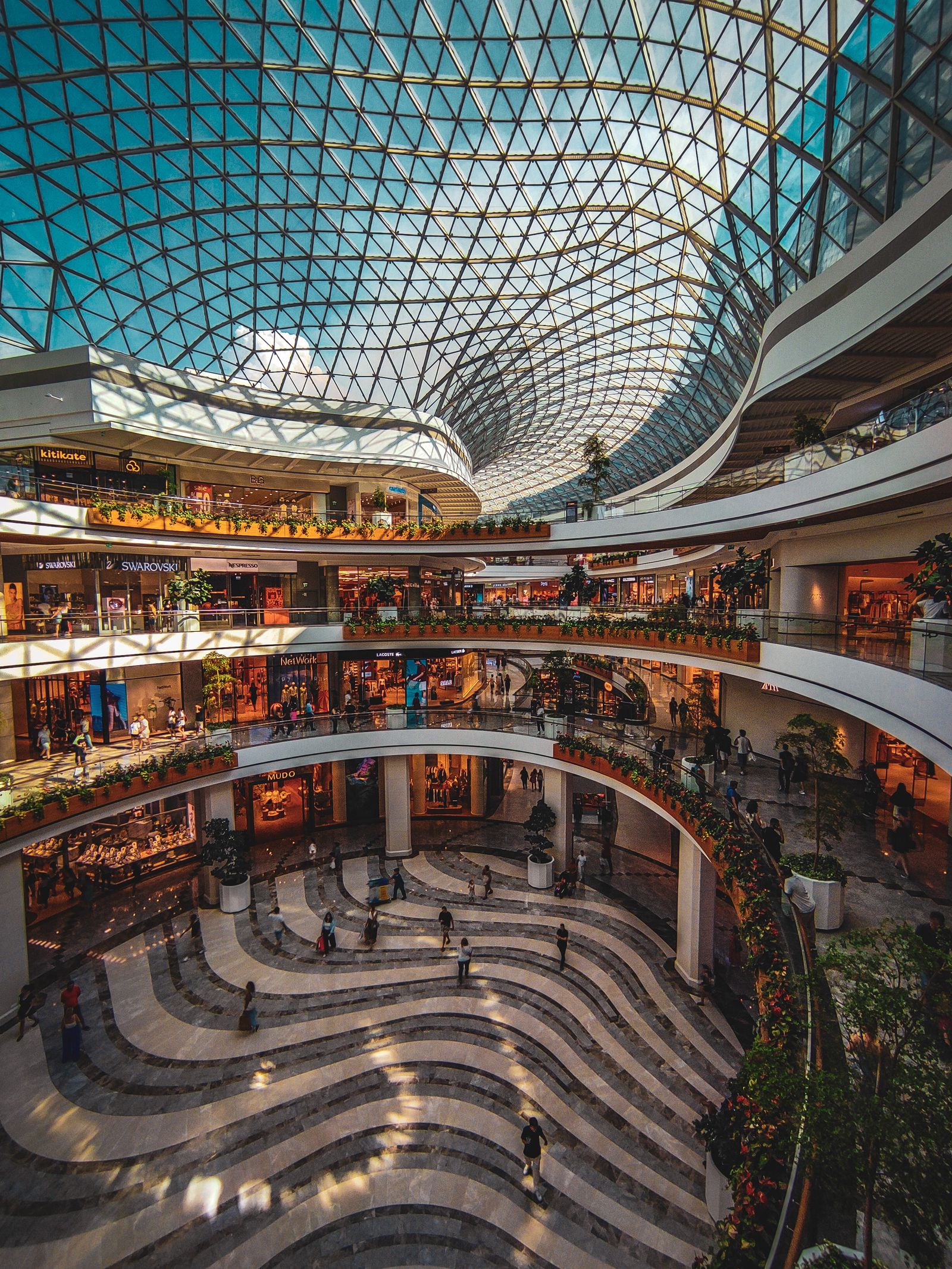 Interior of a modern multi-level shopping mall with a large glass atrium ceiling