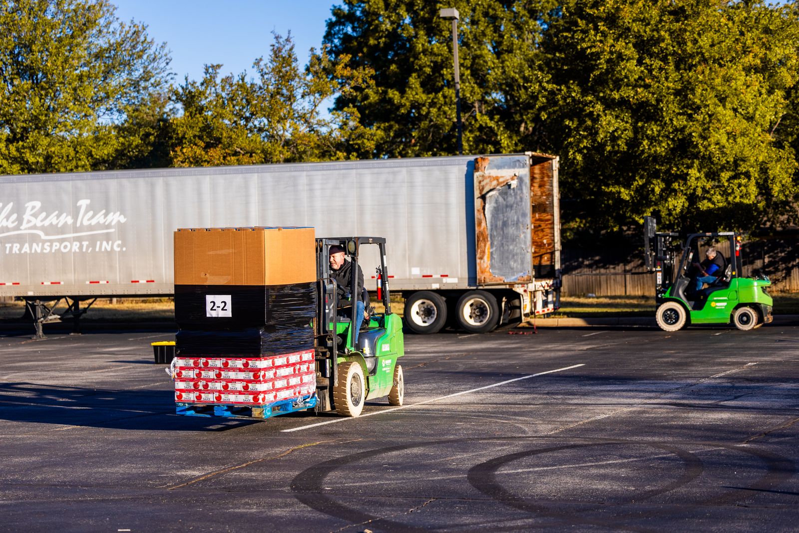 Forklift operators loading pallets next to a semi-truck trailer in a warehouse loading yard