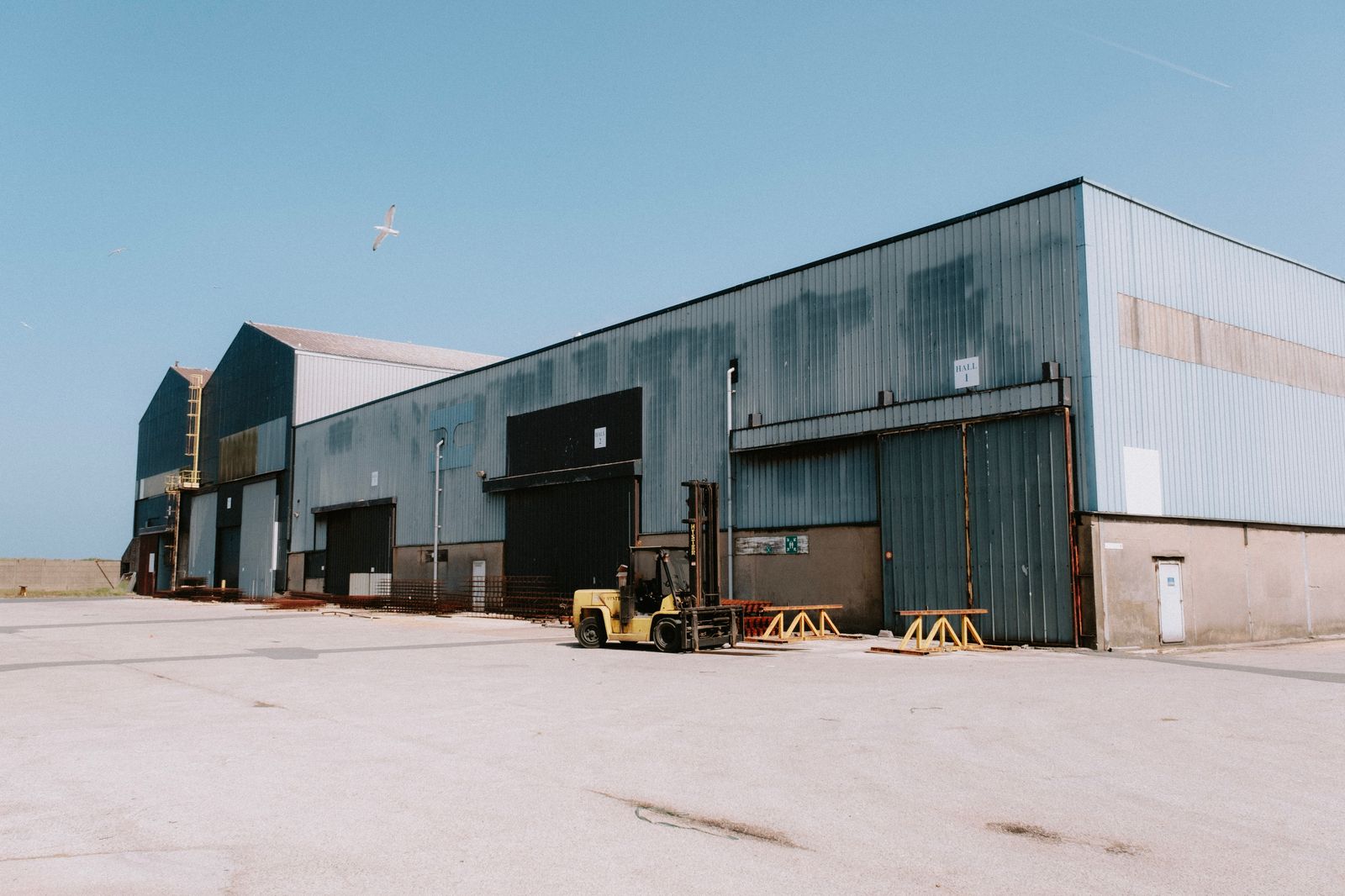Exterior of a large industrial warehouse building with a forklift parked outside