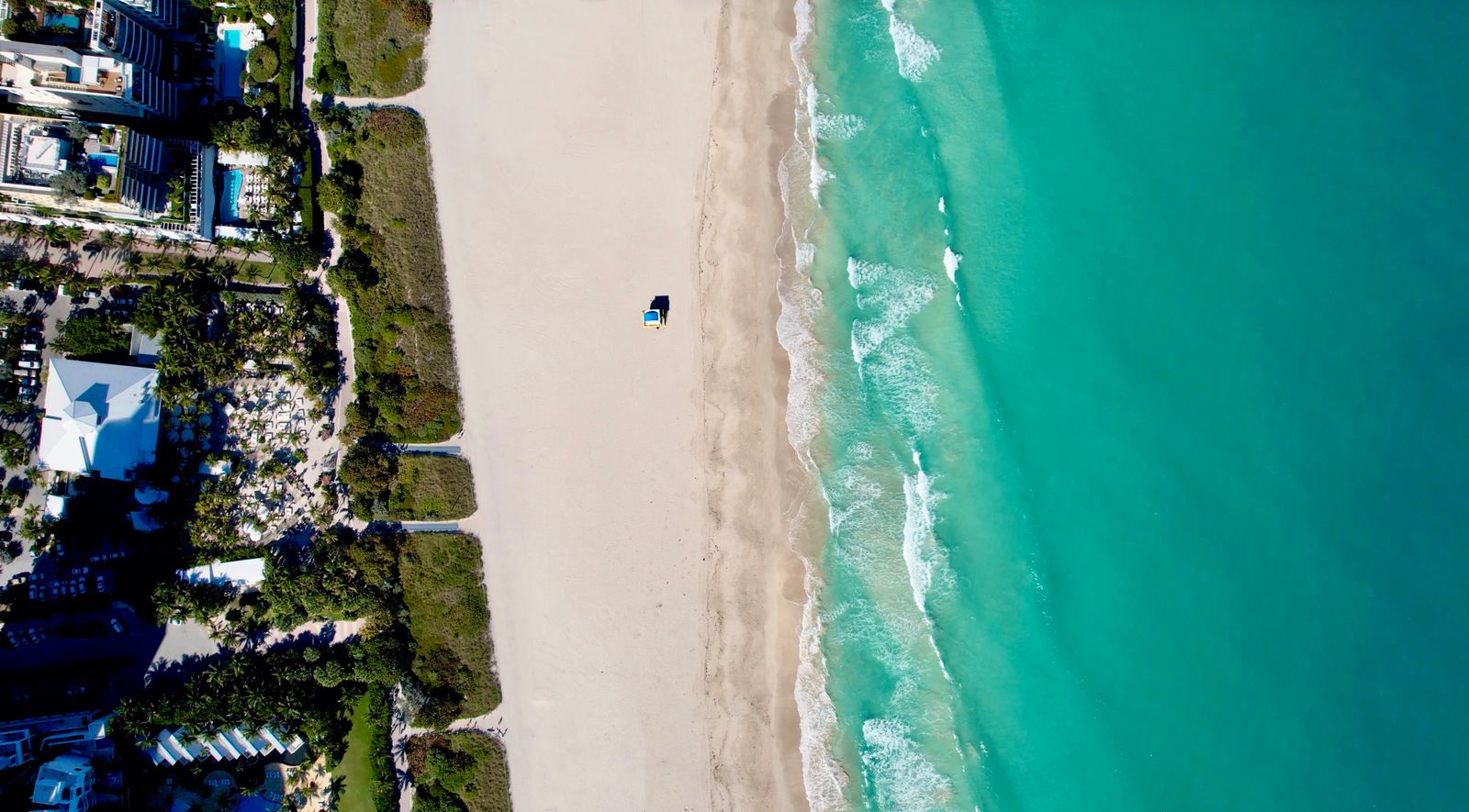 Aerial view of a Miami-area beach with turquoise ocean water, white sand, and beachfront hotels