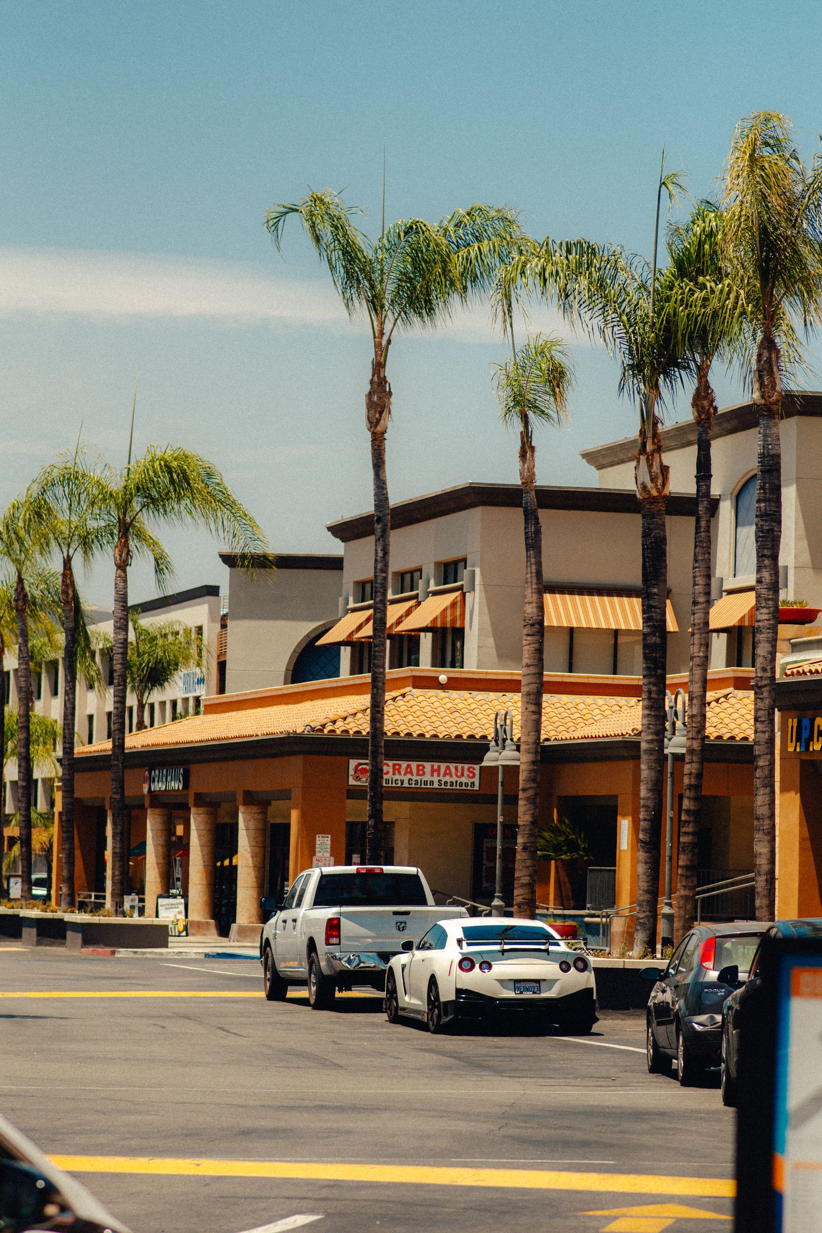 Sunny commercial plaza with a Spanish-tile roofline, palm trees, and storefronts