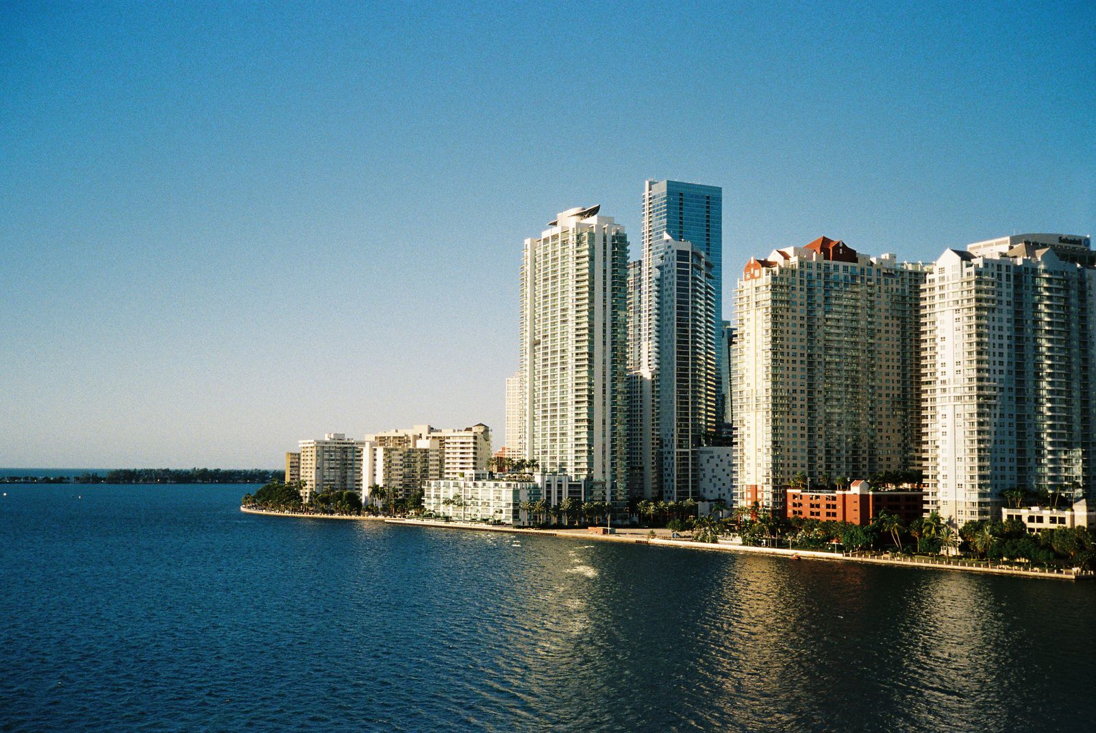 Waterfront high-rise condominium towers along a Miami-area bay under a clear blue sky